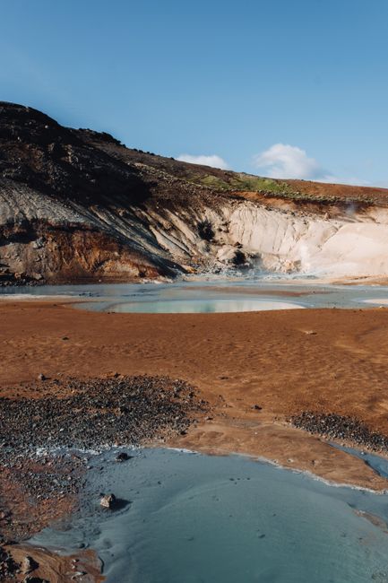 Explore a geothermal landscape featuring blue mineral pools, rocky hills, and a sunlit backdrop.
