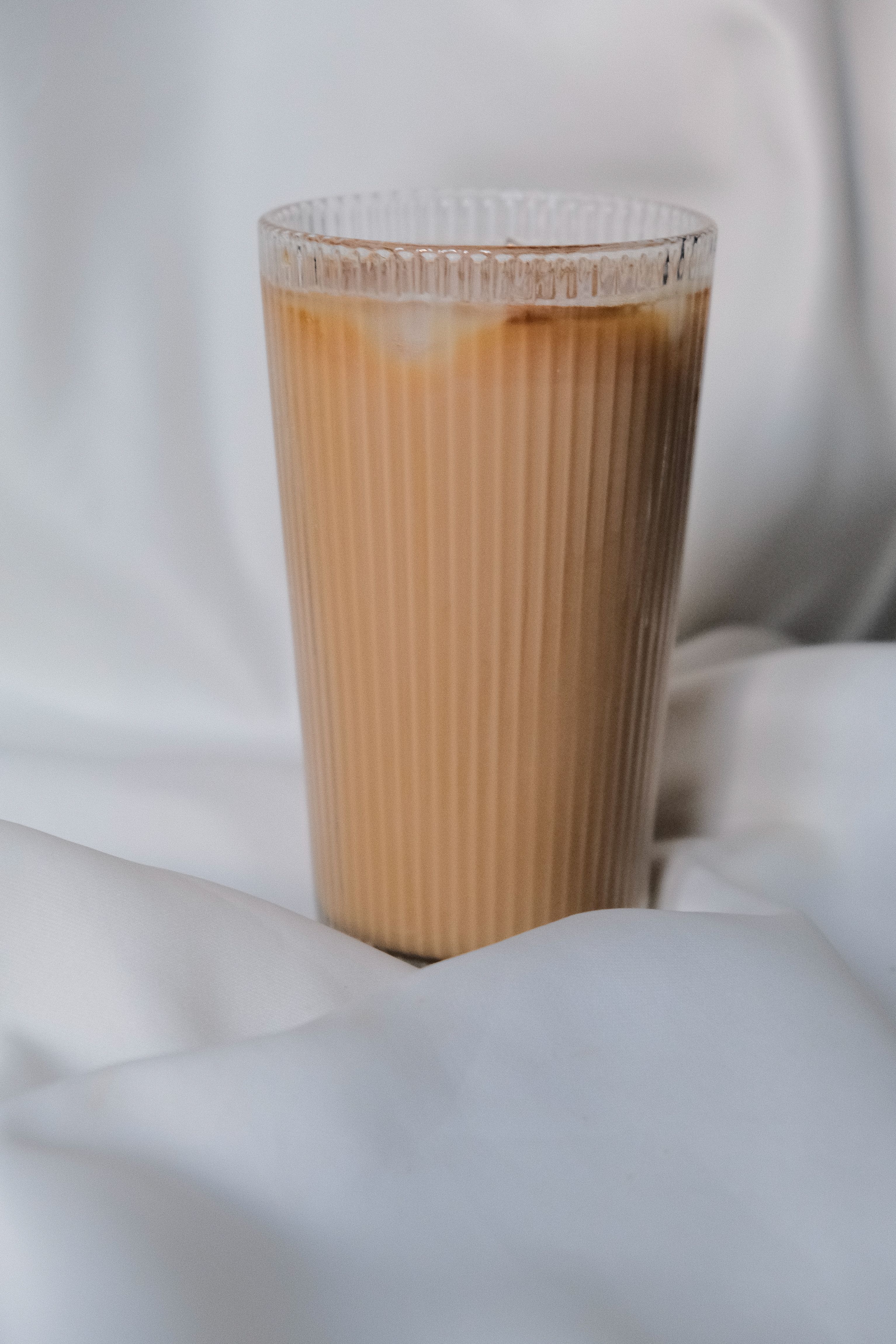 Layered milk coffee in a tall ribbed glass on pale linen — photo by Khadijah Karaca on Pexels