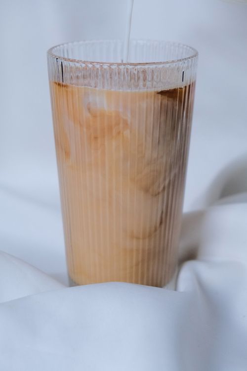 Free Close-up of iced coffee with cream swirling in a ribbed glass against white fabric backdrop. Stock Photo
