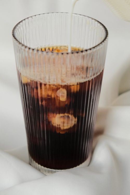 Free Close-up of iced coffee with milk pouring into a glass on a white background. Stock Photo