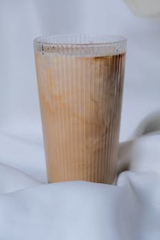 A refreshing iced coffee in a ribbed glass against a soft white fabric background.