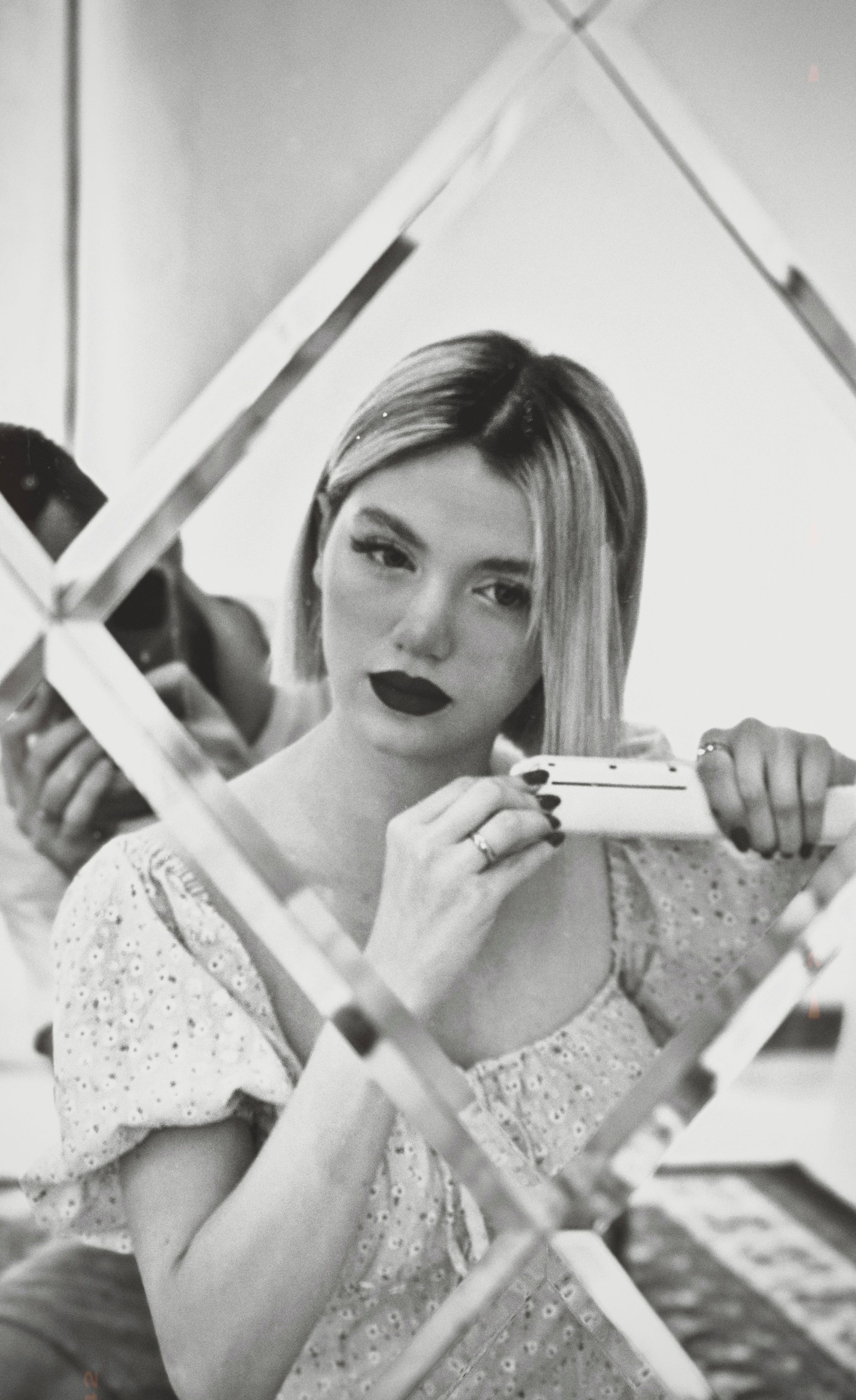 Monochrome portrait of a woman grooming hair in front of a mirror, showcasing fashion and style.