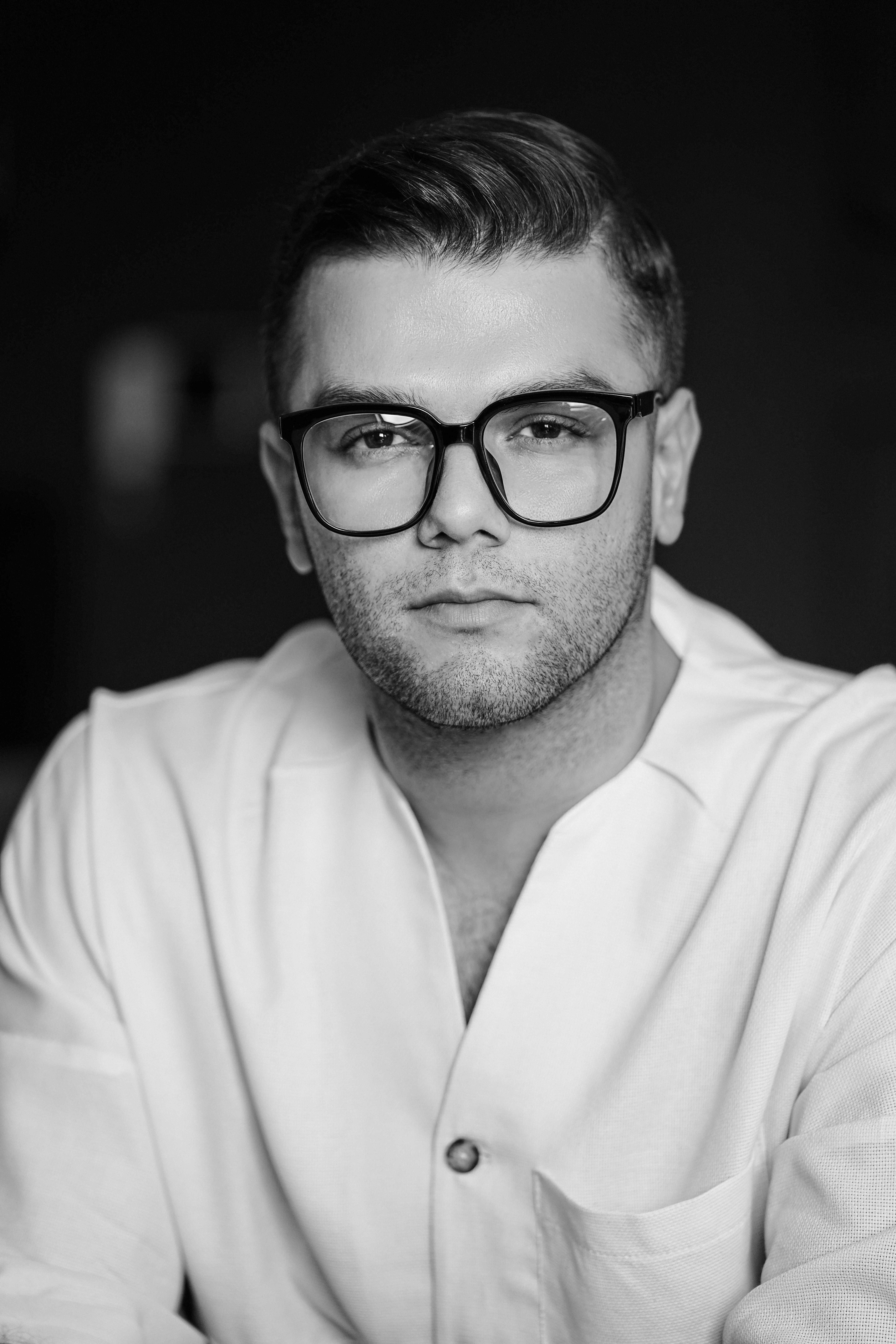 Elegant black and white portrait of a man wearing eyeglasses and white clothing.
