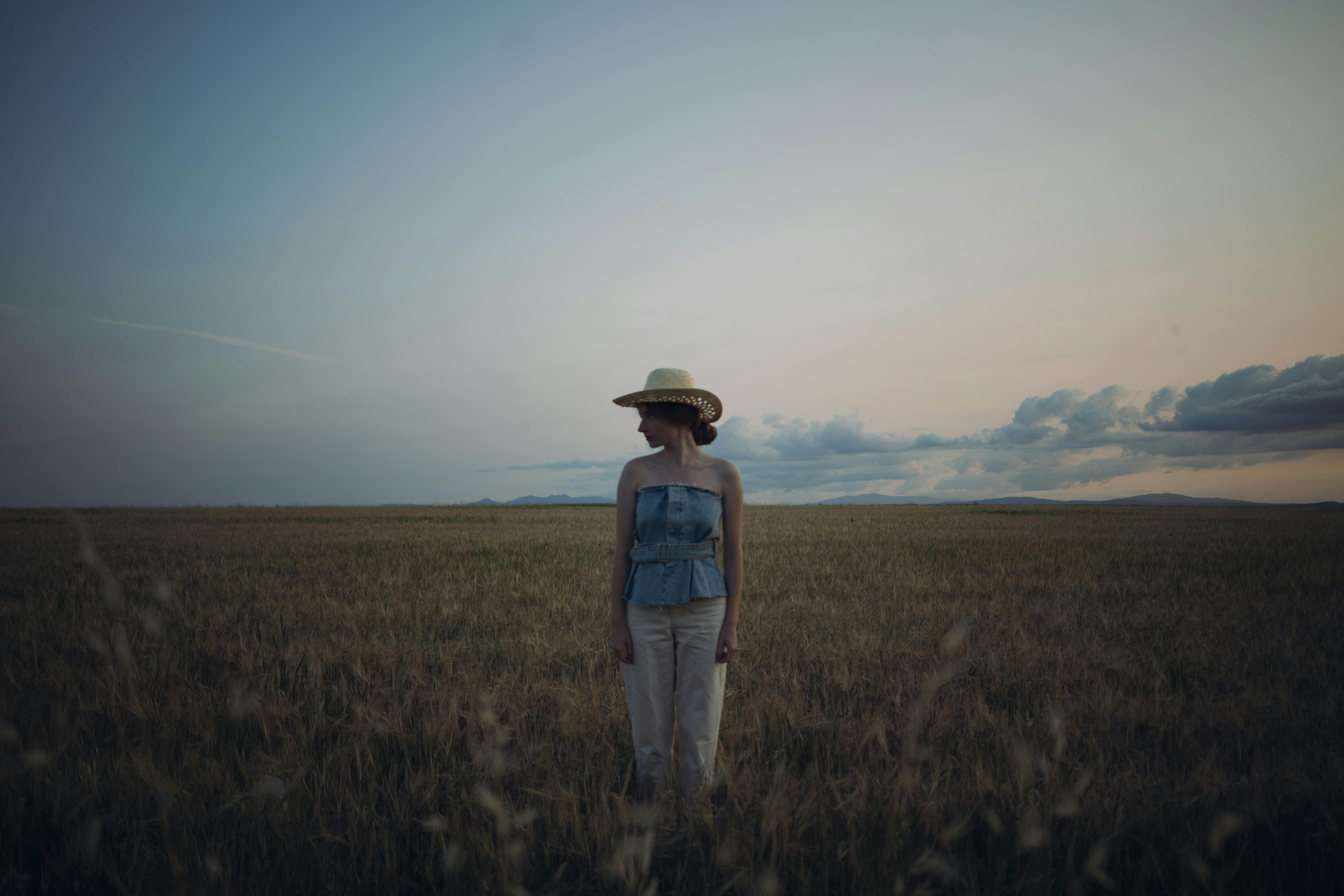Calm woman wearing hat in wheat field at twilight, embracing nature's tranquility.