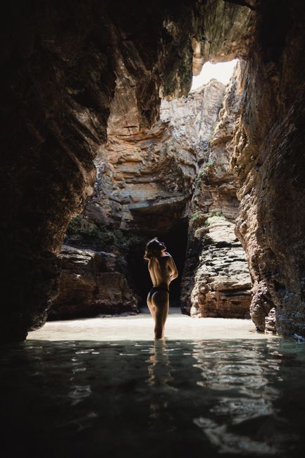 A woman stands in a sunlit cave pool, highlighting natural beauty and serenity.