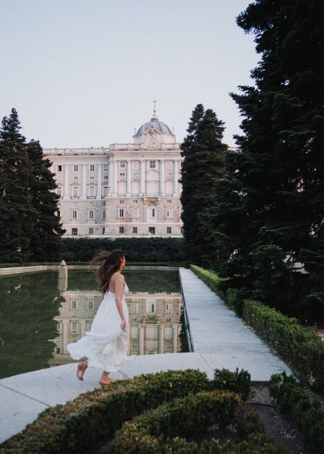 Woman in white dress walking near the Royal Palace with reflection in Sabatini Gardens, Madrid.