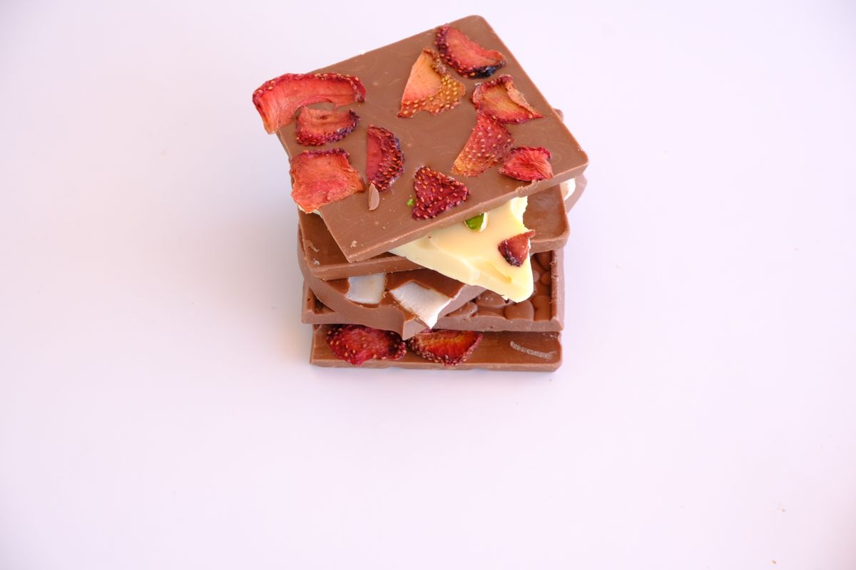 A delicious stack of milk chocolate bars topped with dried strawberries on a white background.