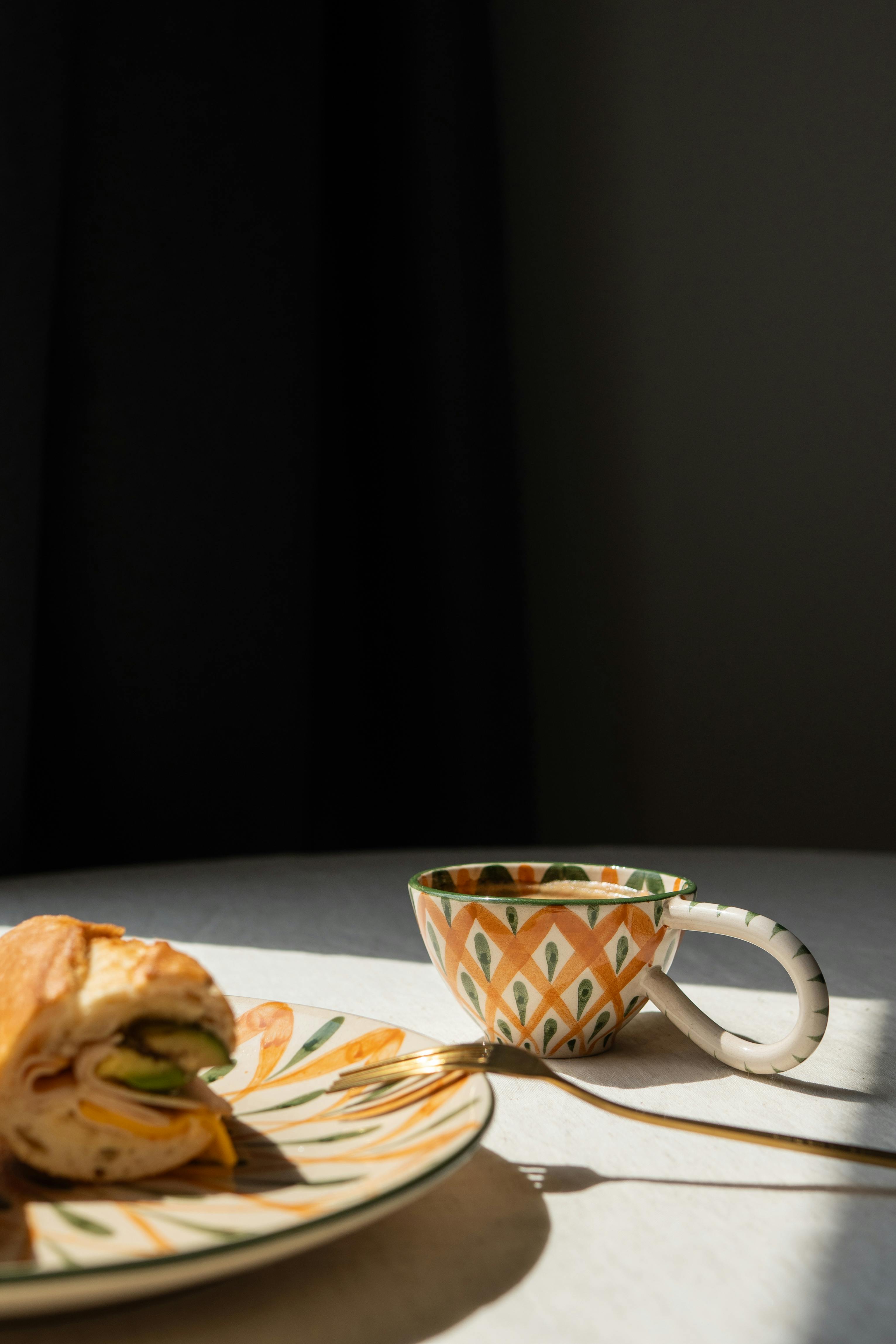 Close-up of a sandwich and coffee on a patterned plate in natural light.