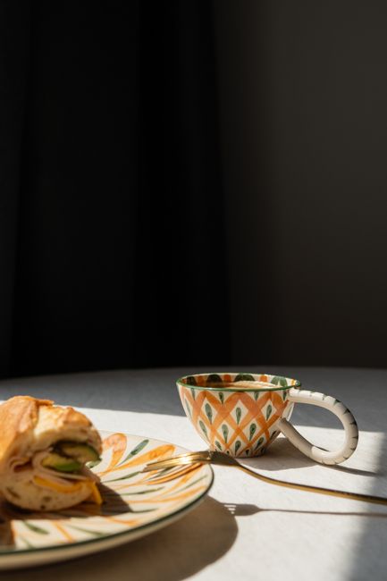 Close-up of a sandwich and coffee on a patterned plate in natural light.