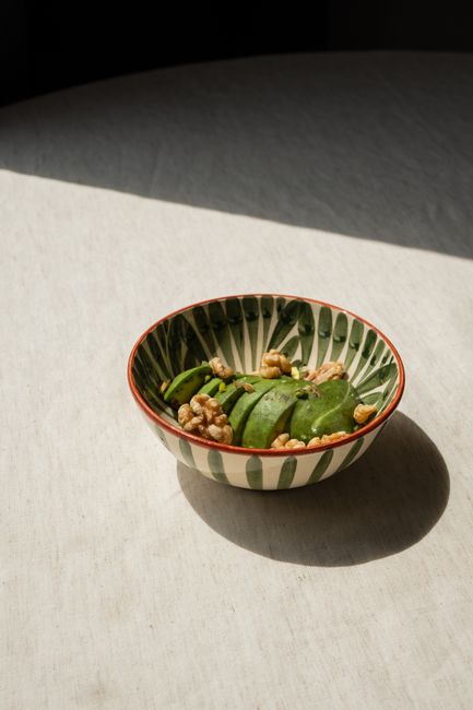 Minimalist shot of sliced avocado with walnuts in a stylish bowl on a sunlit table.