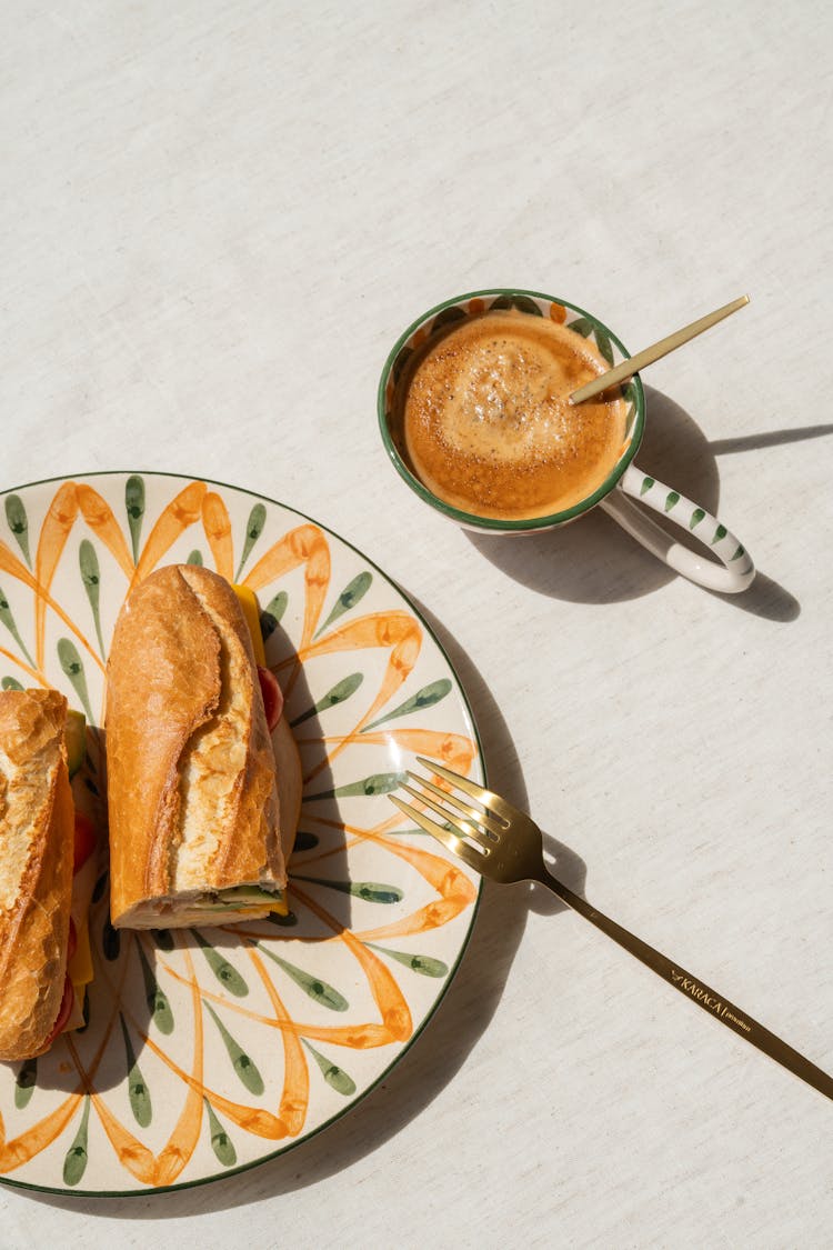 A Baguette Sandwich On A Plate And A Cup Of Coffee 