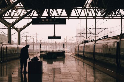 Free A silhouette of a man standing at Yichangdong Railway Station with trains and a rainy urban backdrop. Stock Photo