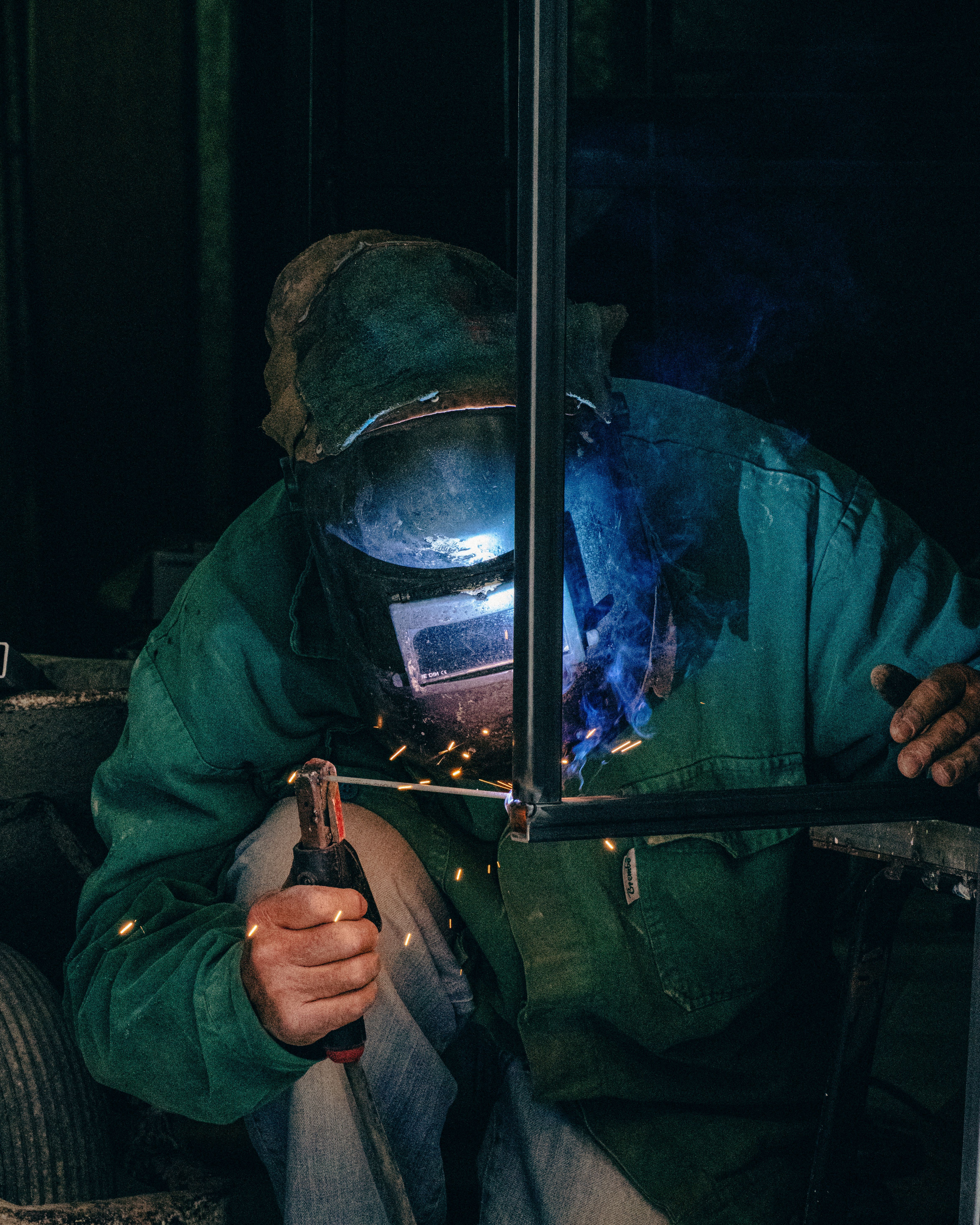 Welder using equipment in a Mellieħa workshop, garbed in safety gear with welding sparks.