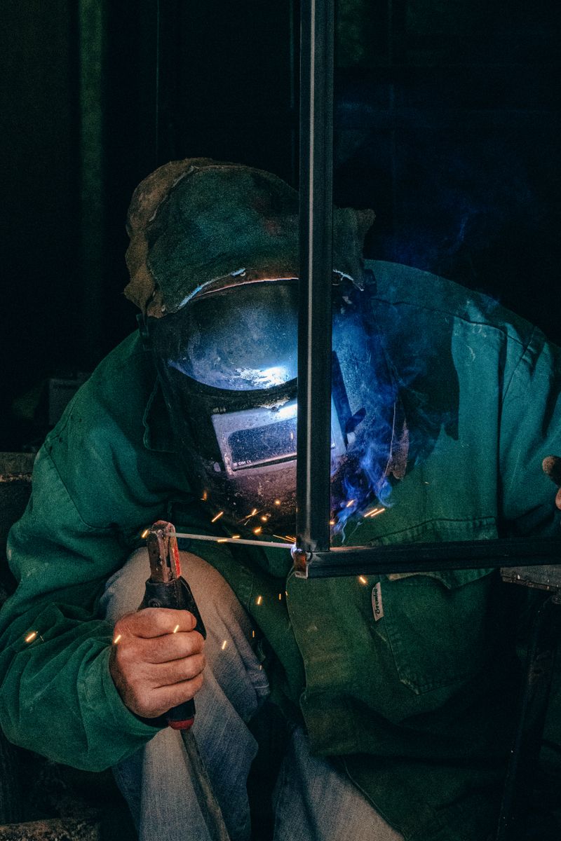 Welder using equipment in a Mellieħa workshop, garbed in safety gear with welding sparks.