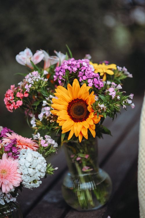 Free Beautiful vibrant summer bouquet featuring a sunflower in a glass vase on a table. Stock Photo