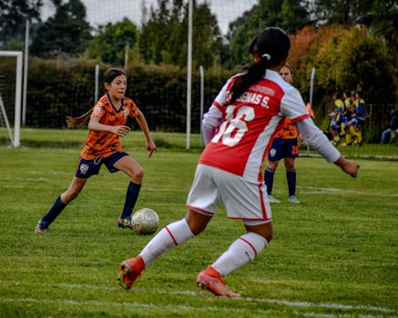 Girls playing soccer on a green outdoor field during a competitive match.
