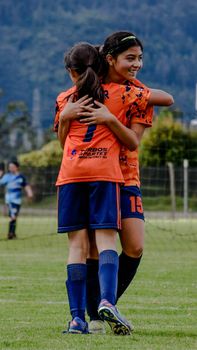 Young girls embrace in celebration during an outdoor soccer match, showcasing teamwork and sports spirit.