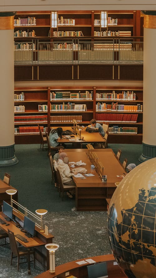 People Sitting at the Table in a Library and Studying