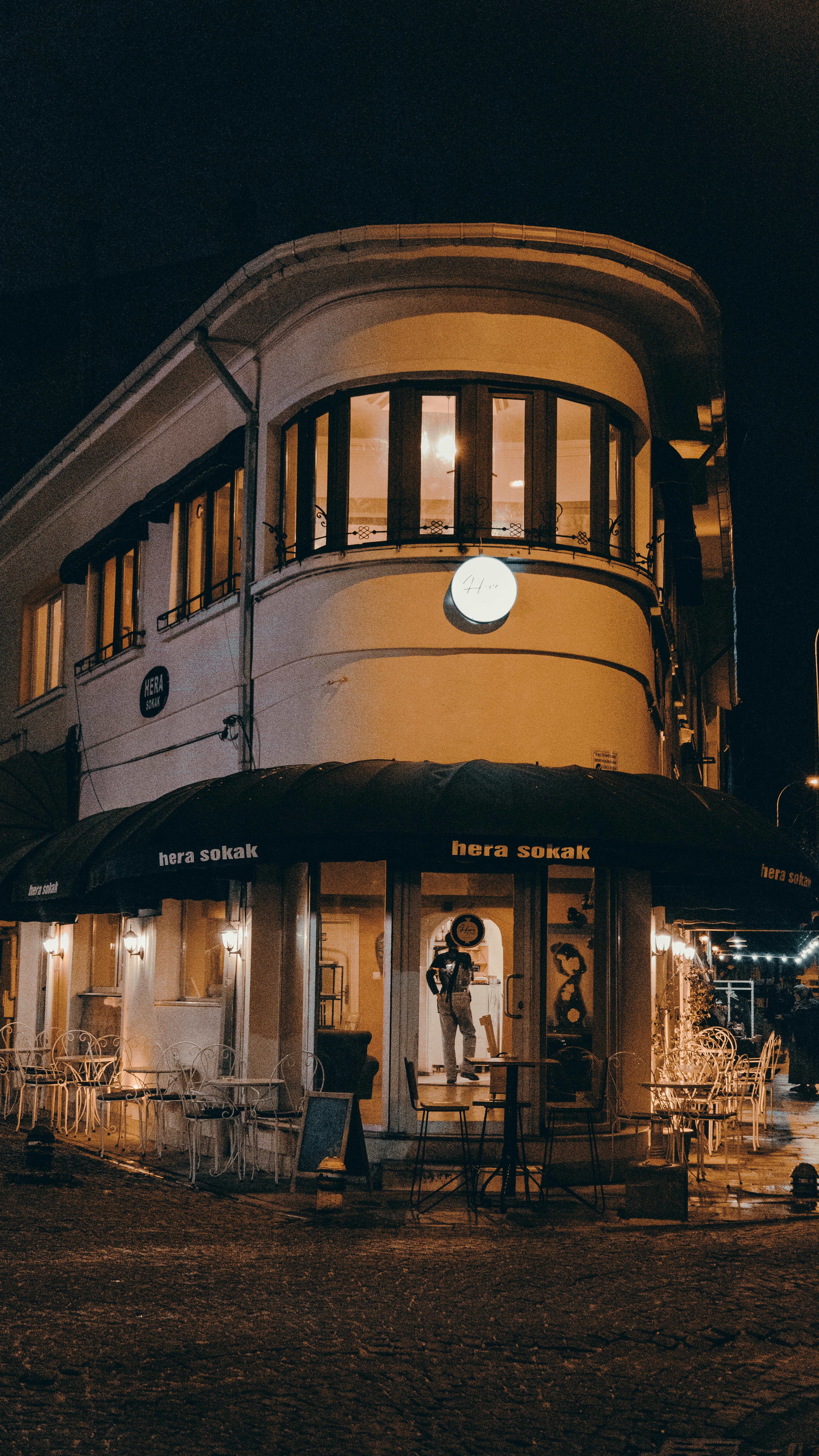 Free Illuminated café on a cobblestone street at night showcasing urban architecture. Stock Photo