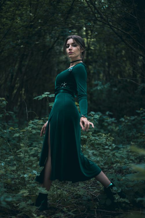 Free A woman in a green dress poses elegantly in a lush forest, capturing a blend of fashion and nature. Stock Photo