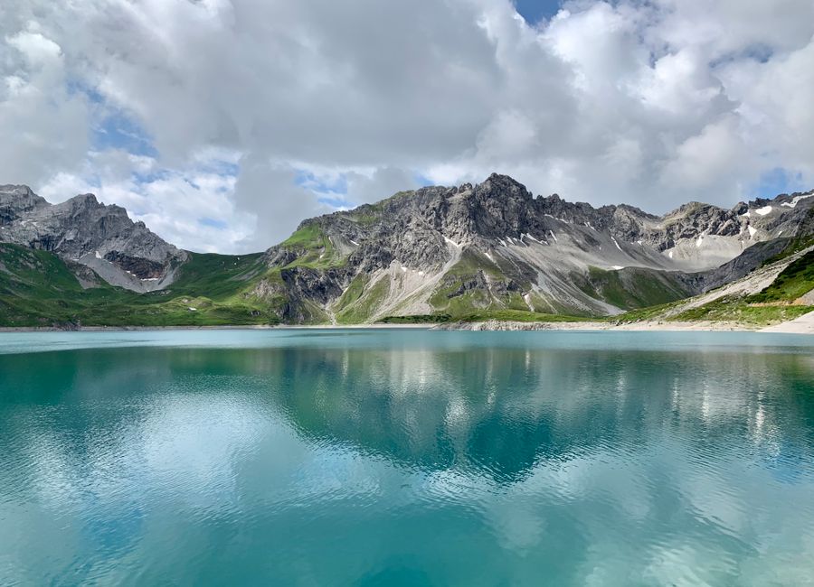 A stunning view of a turquoise mountain lake reflecting clouds in Vorarlberg, Austria.