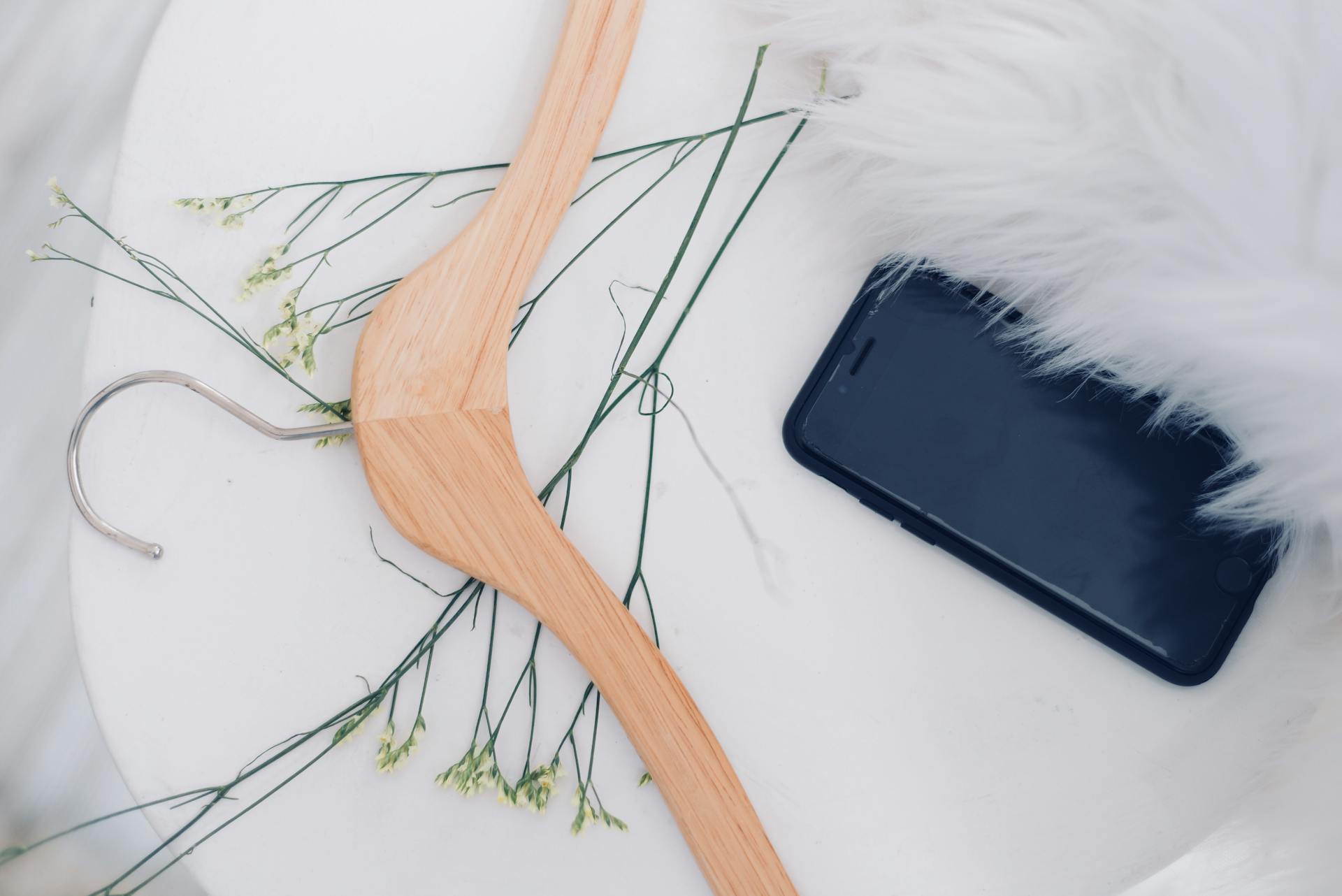 Elegant flat lay featuring a hanger, smartphone, and faux fur on a white surface.