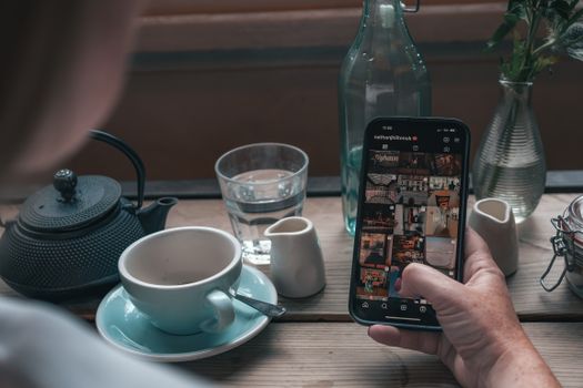 A person browsing Instagram on a smartphone in a cozy Manchester café setting with tea and glassware.