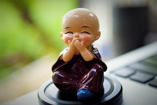 一个表情快乐的可爱陶瓷和尚雕像，坐在一台模糊的笔记本电脑表面