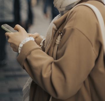 Close-up of a woman in a coat using a smartphone on an urban street.