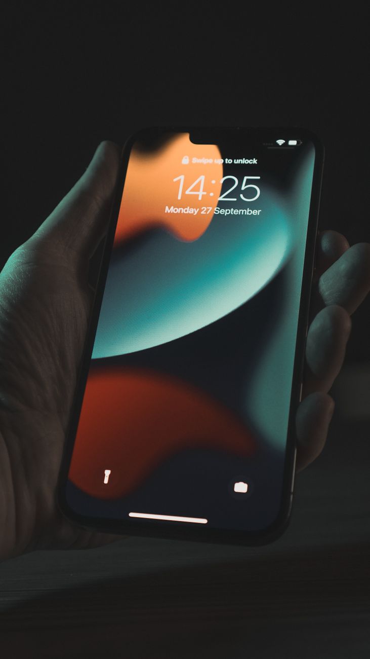 Close-up of a hand holding a smartphone displaying the lockscreen and time in a dimly lit setting.