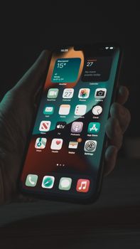 A close-up view of a hand holding a smartphone displaying various app icons, taken at night.