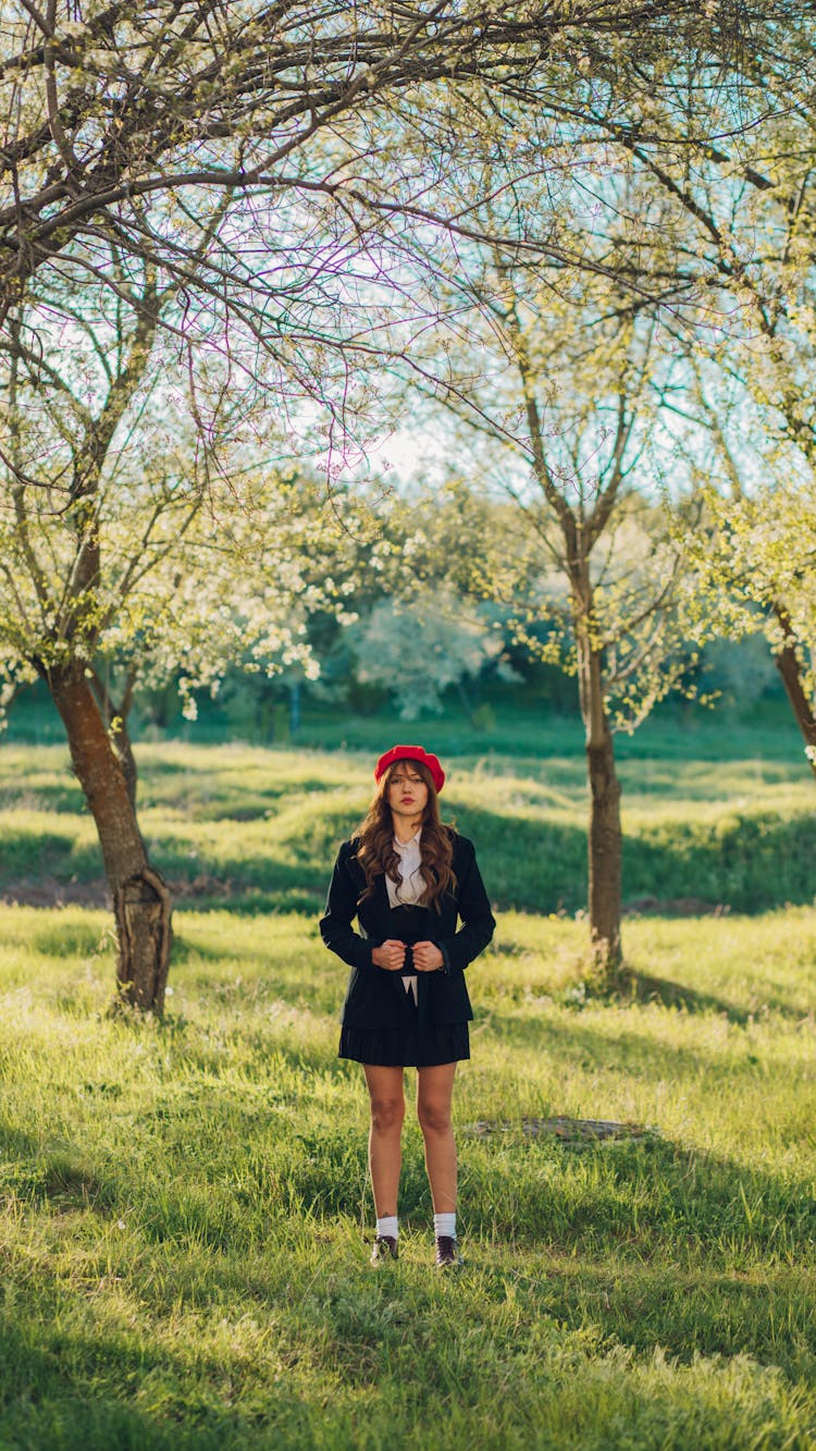 Young Woman In Coat, Mini Skirt, And Red Beret Posing In A Spring Park