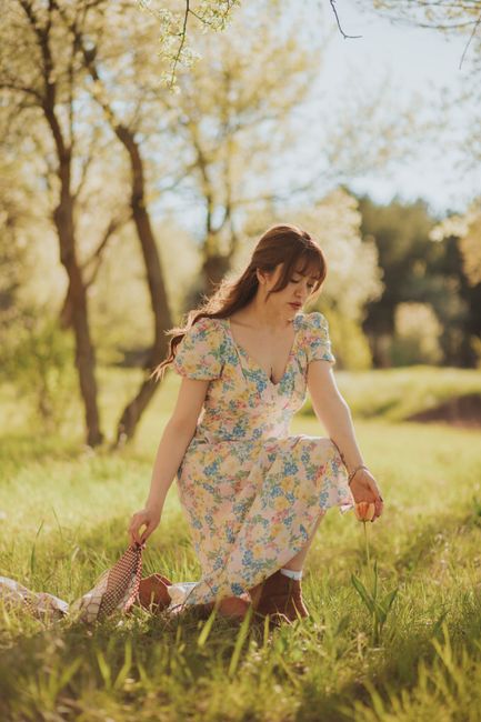 A woman in a floral dress kneels in a sunlit garden, embracing the beauty of spring.