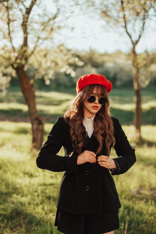 Free Elegantly dressed woman wearing a red beret standing in a sunlit park. Stock Photo