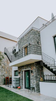 Contemporary house exterior with stone cladding and metal staircases, showcasing modern architecture.