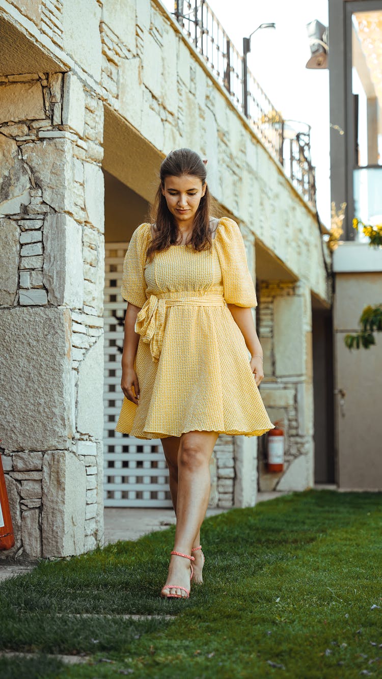 Young Woman In Yellow Dress Walking On Grass