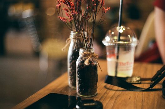 Warm café scene featuring decorative jars with coffee beans and a glass with straw on a wooden table.