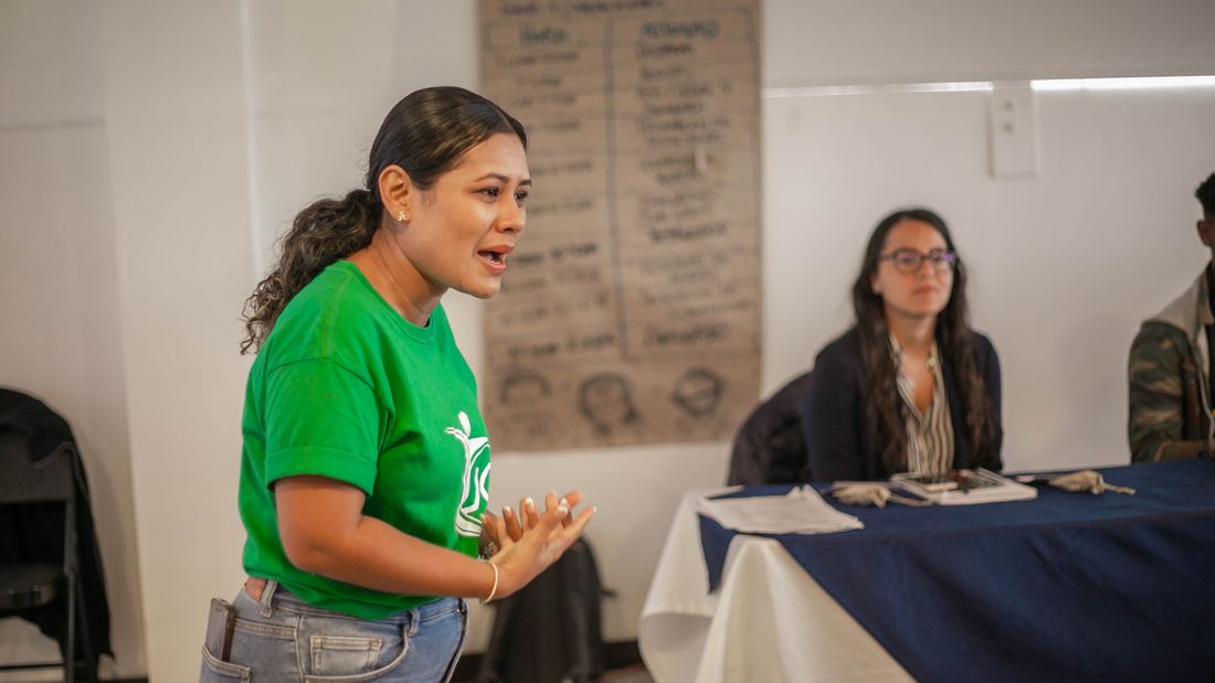 A young woman speaking with conviction to a group seated around her.