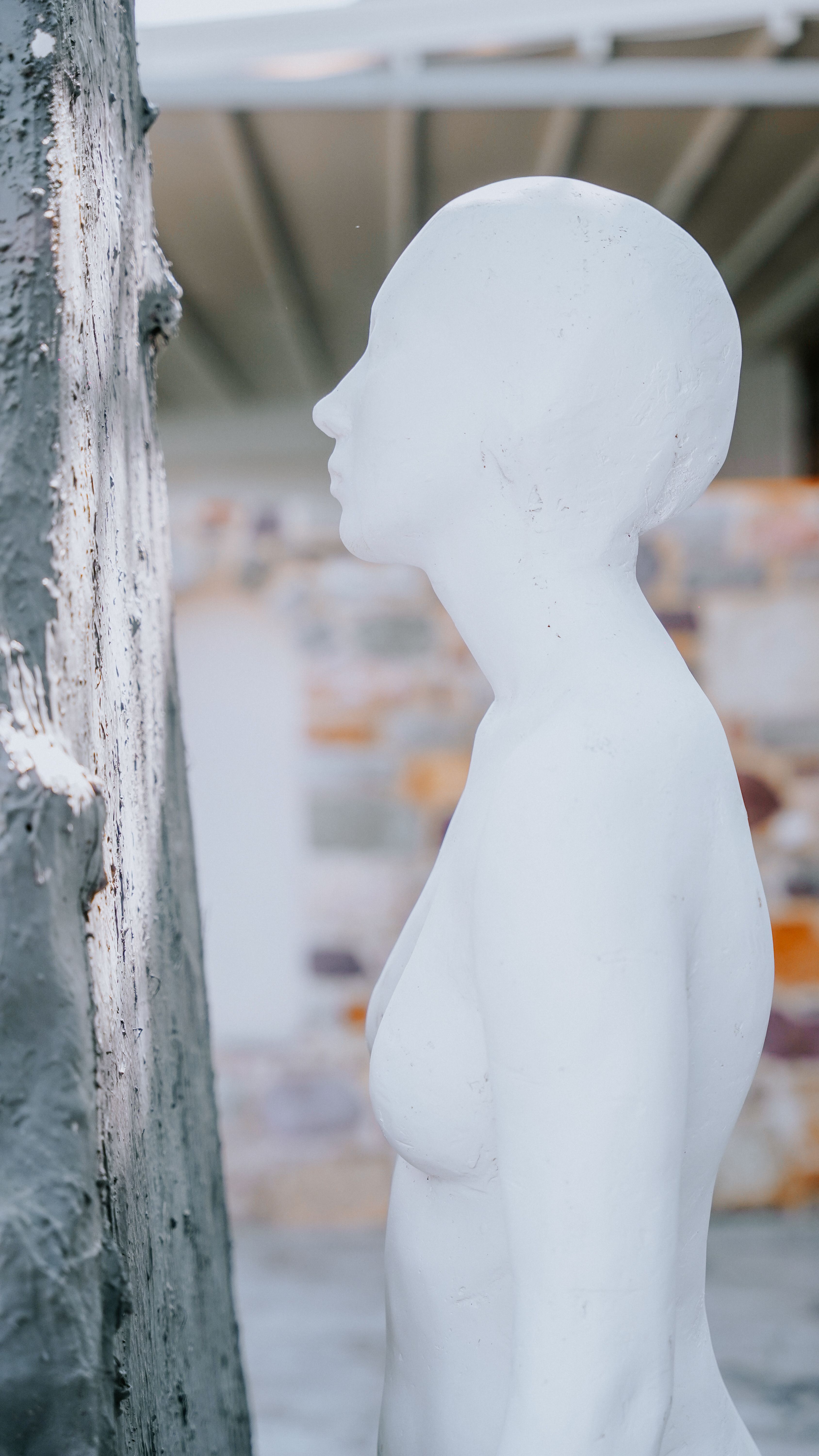 Contemporary white sculpture in profile view, indoors with a backdrop of blurred artwork.