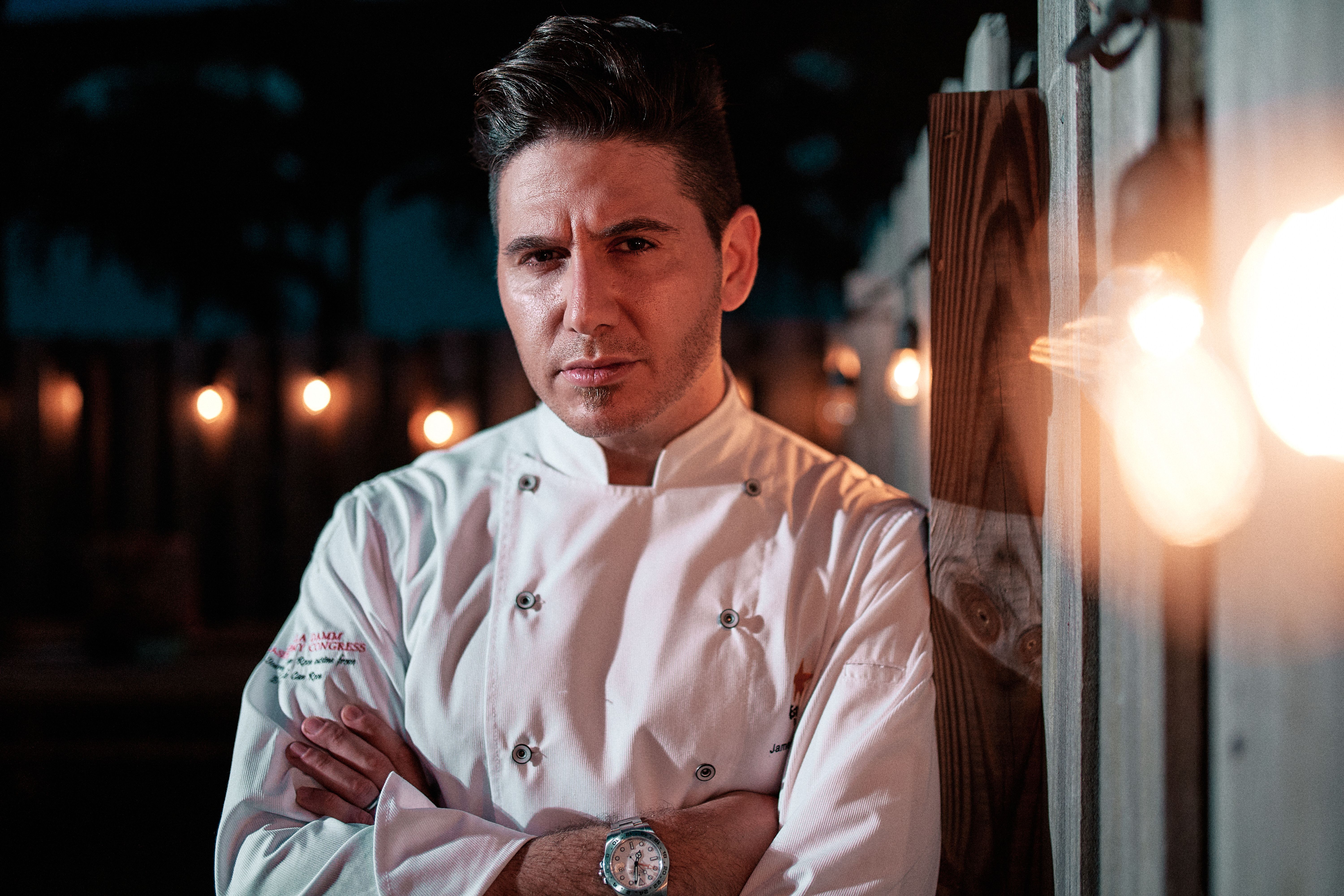 A confident chef poses with arms crossed at night in Miami, showcasing culinary expertise. | BocaVibe