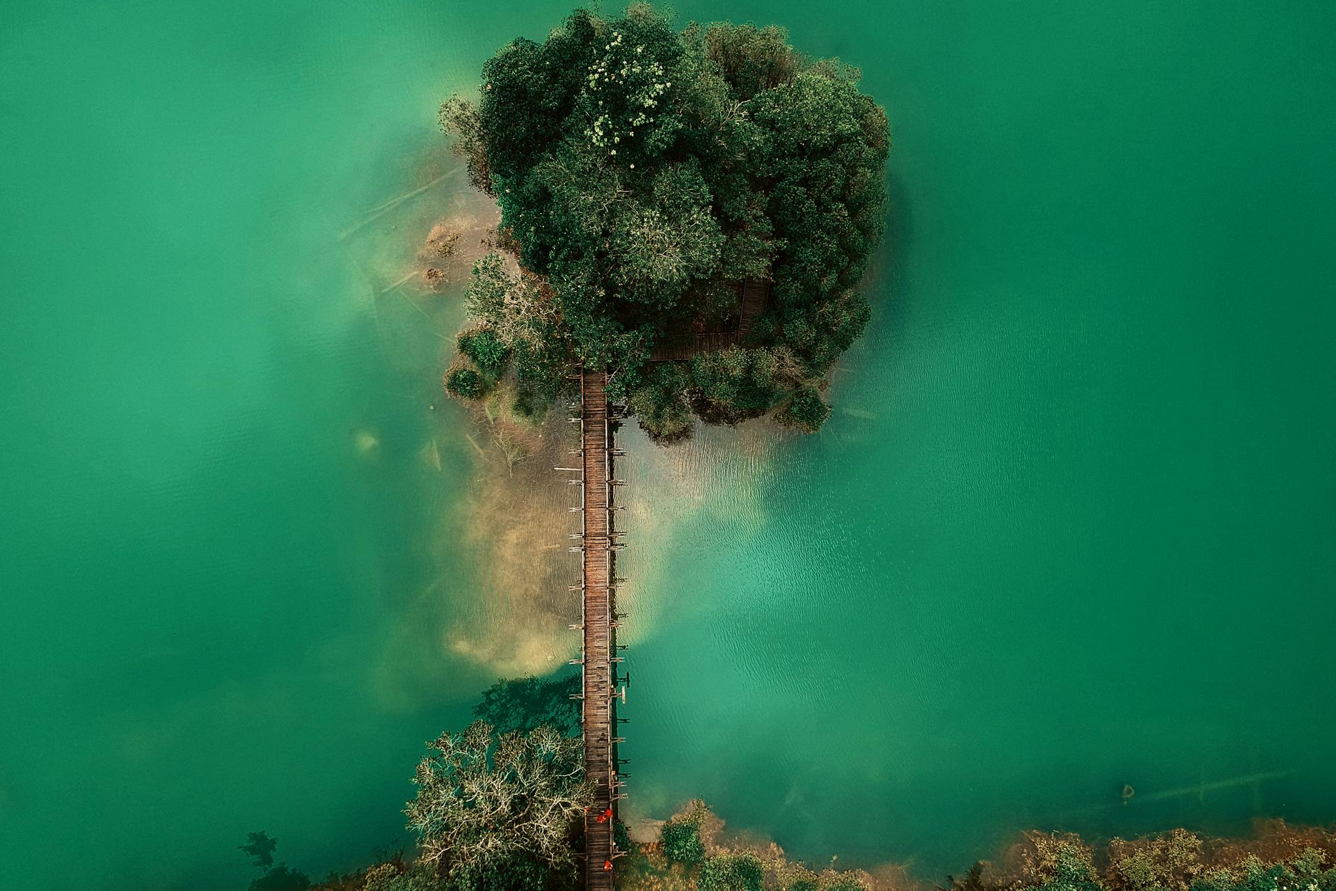 Stunning aerial shot of a wooden bridge leading to a tree-covered island in vibrant green waters.