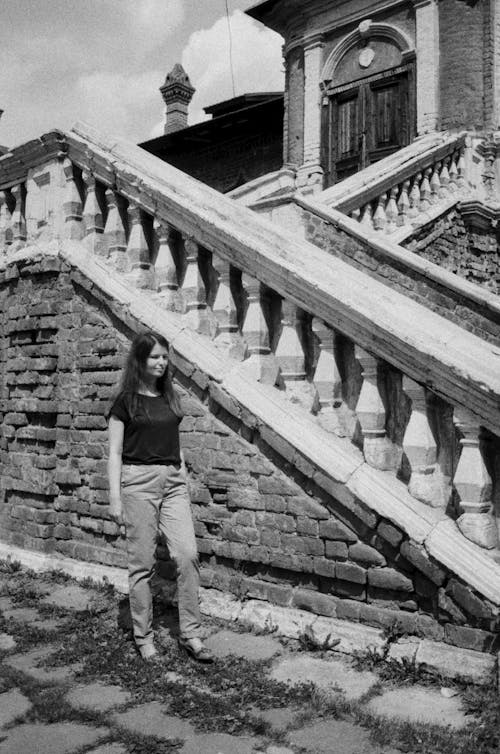 Black and White Picture of a Woman Standing in front of an Antique Building 