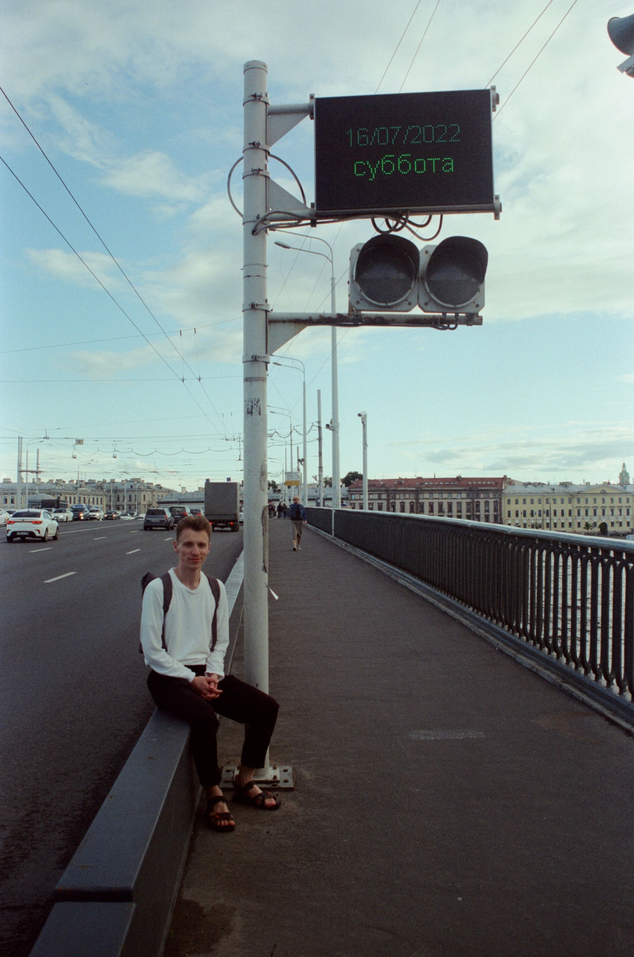 A man sits on a city bridge with a sign in the background, capturing an urban travel moment.