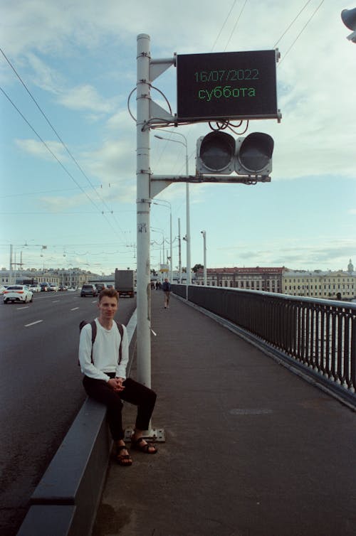 Young Man Sitting by the Road on the Bridge 