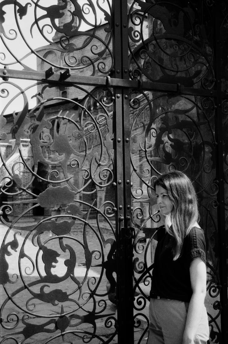 Young Woman In Black T-shirt Posing By Ornately Decorated Iron Gates