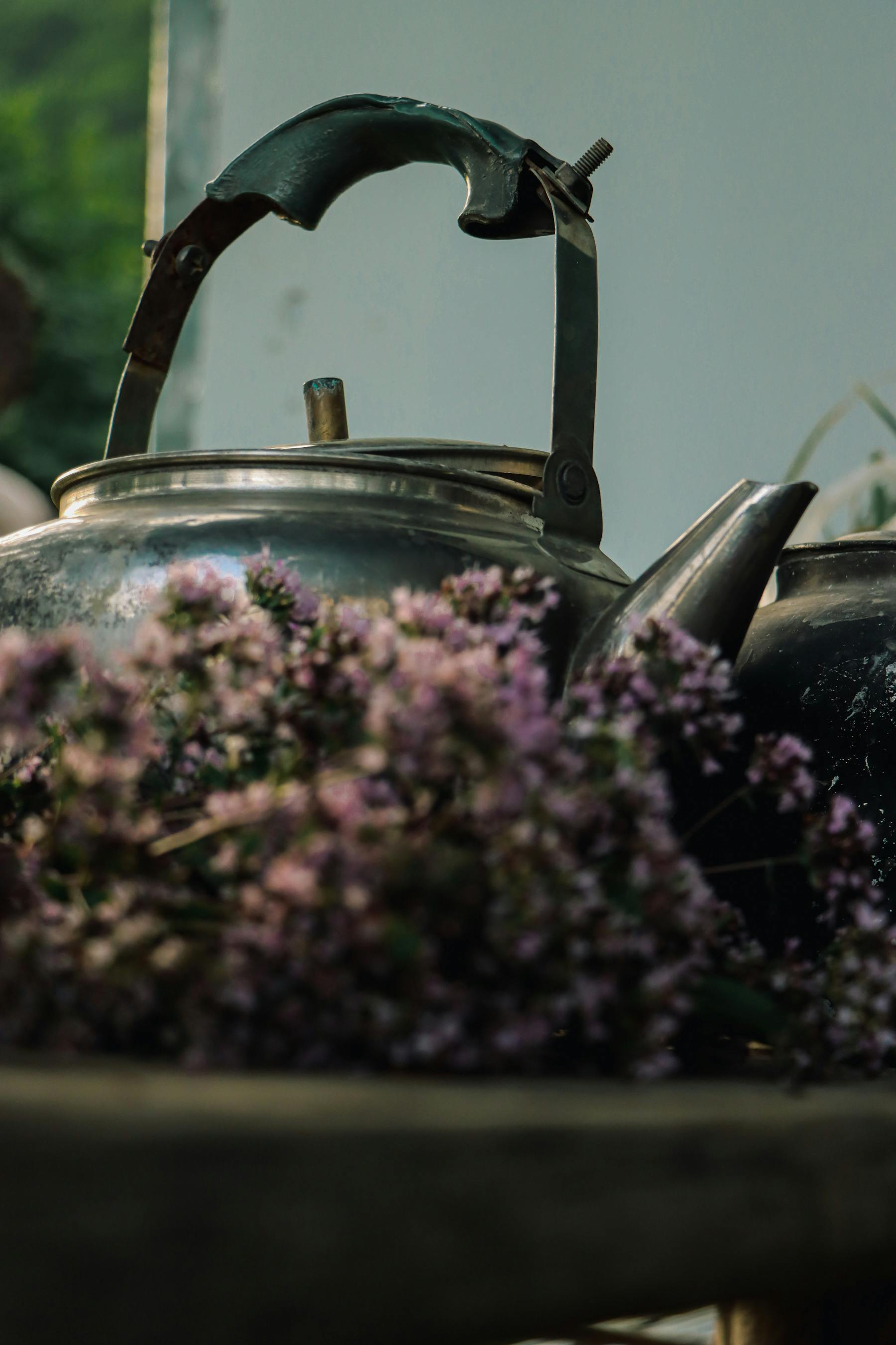 a silver tea pot and some purple flowers