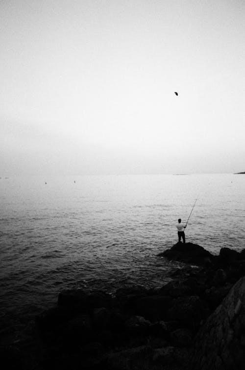 Black and White Picture of a Man Fishing on the Shore 