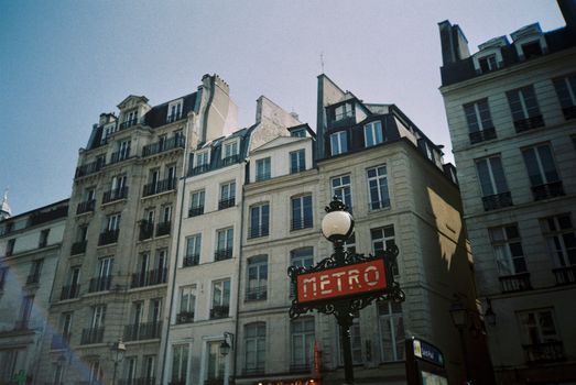 Classic Paris residential buildings with a vintage metro sign under clear skies.
