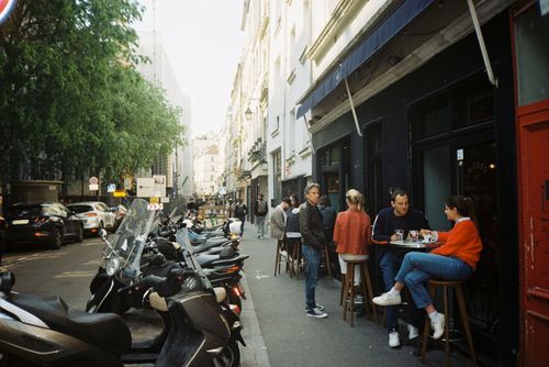 Free People dining outdoors on a vibrant European street with scooters parked nearby. Stock Photo