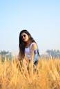 一位戴着太阳镜的年轻女子在金色的田野里，享受着阳光明媚的一天，捕捉着休闲与时尚的瞬间